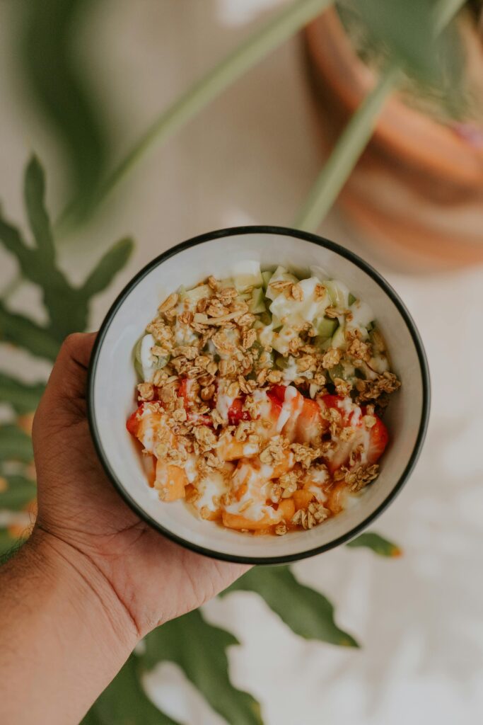 Delicious bowl of granola, fruit, and yogurt held in hand with greenery backdrop.
